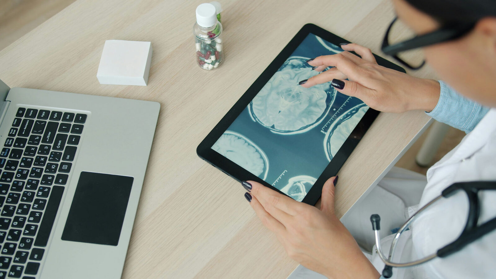 Clinician in a lab coat reviewing brain scan images on a tablet