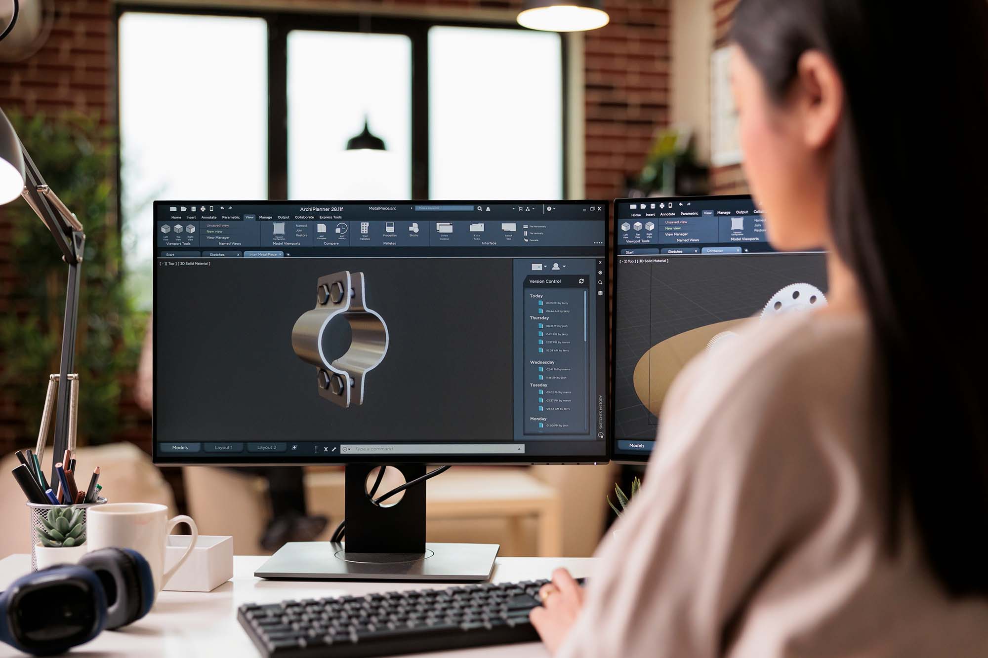 Engineer reviewing a 3D CAD model of a bolted metal clamp on dual monitors at a desk