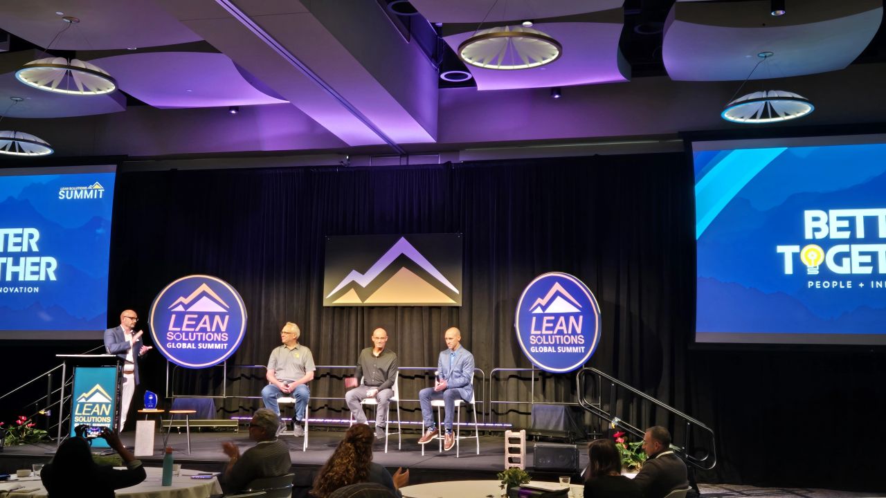 Stage at the LEAN Solutions Global Summit with Better Together: People + Innovation on the screens and a speaker at the podium before the audience
