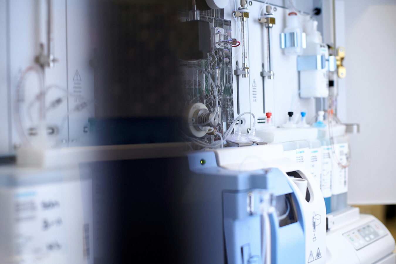 Close-up of diagnostic lab equipment showing tubing, fluid reservoirs, and a control panel