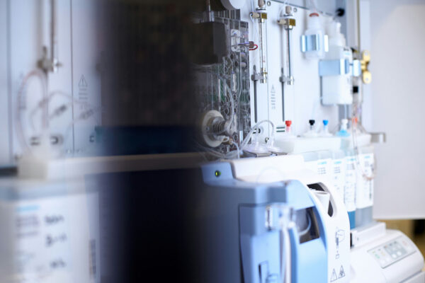 Close-up of diagnostic lab equipment showing tubing, fluid reservoirs, and a control panel