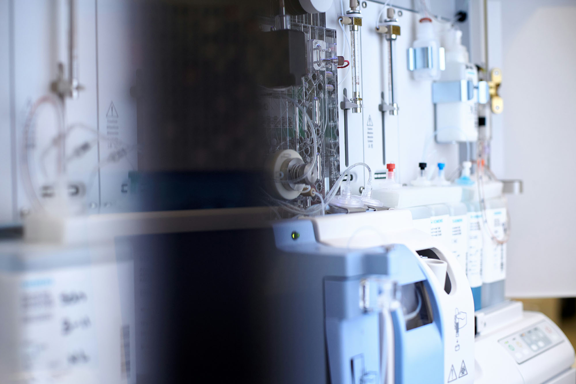 Close-up of diagnostic lab equipment showing tubing, fluid reservoirs, and a control panel