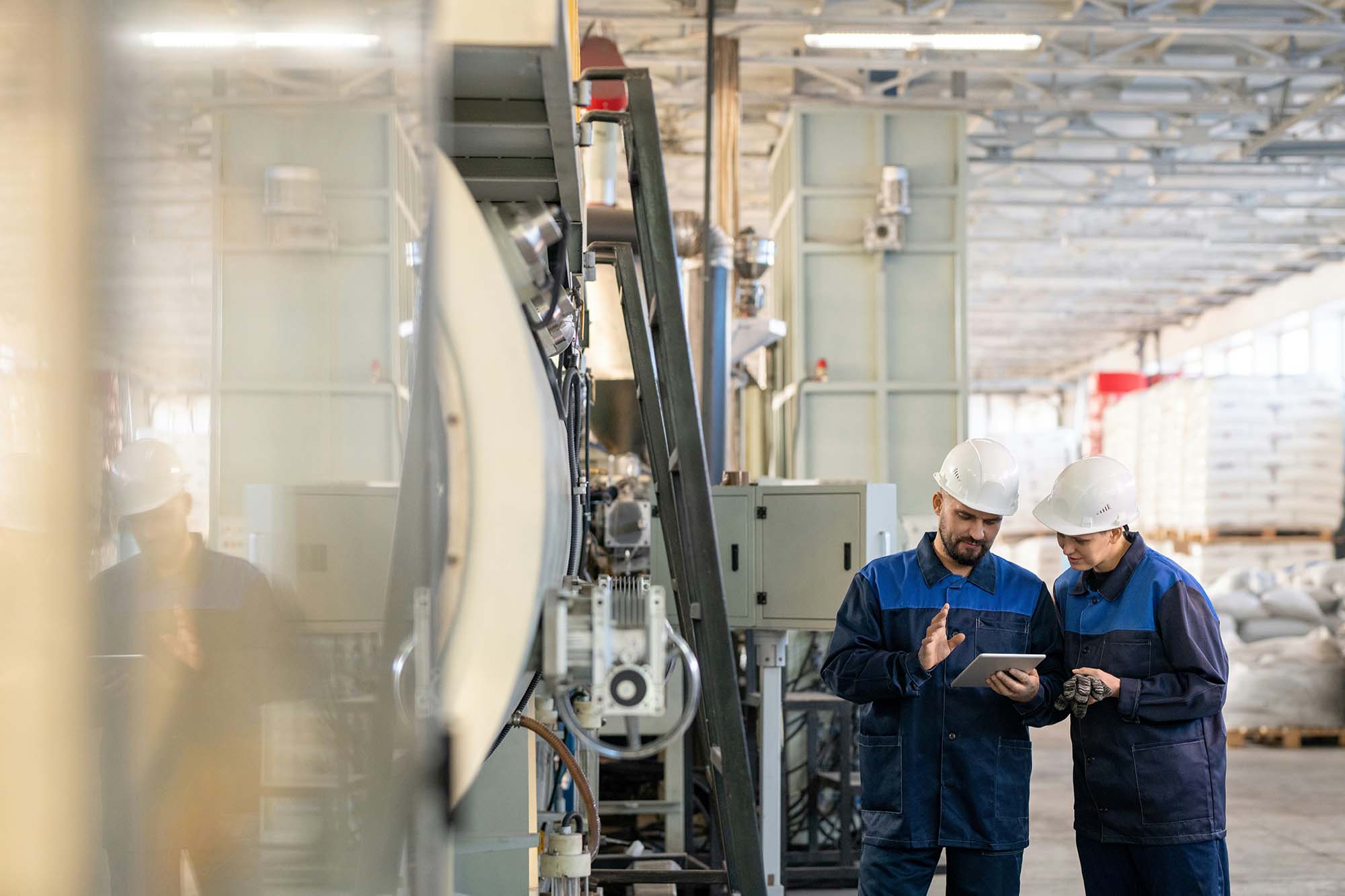 Two engineers in hard hats reviewing a tablet on a manufacturing plant floor