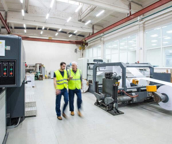 Two workers in yellow safety vests walking past production machinery on a factory floor